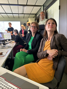 Forstministerin Miriam Staudte und Innenministerin Daniela Behrens sitzen vor Monitoren an einem Schreibtisch, im Hintergrund stehen mehrere Personen.