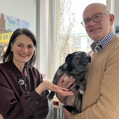 Ein Foto zeigt: Ministerin Miriam Staudte neben ML-Mitarbeiter Heiko Richter. Beide lachen in die Kamera. Herr Richter hält Hündin "Cookie" auf dem Arm.