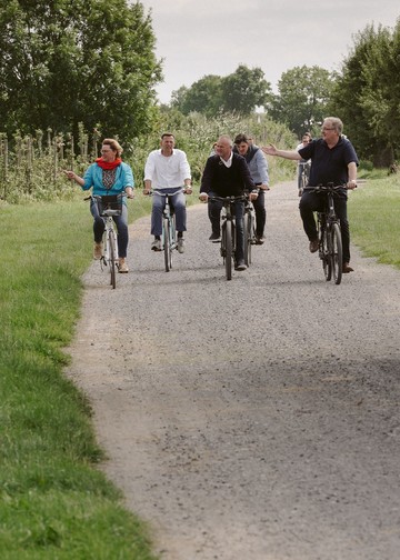 Ministerin Barbara Otte-Kinast fährt zusammen mit einer Gruppe Fahrrad durch ein Obstanbaugebiet.