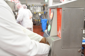 Ein Mitarbeiter in einem fleischverarbeitenden Betrieb hält seine Hände in eine Hygieneschleuse. Ein Licht an der Schleuse leuchtet grün.