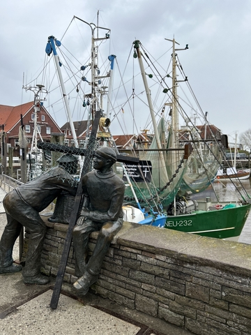 Fischer-Statue an Kaimauer, im Hintergrund ein Schiff mit Fangnetzen