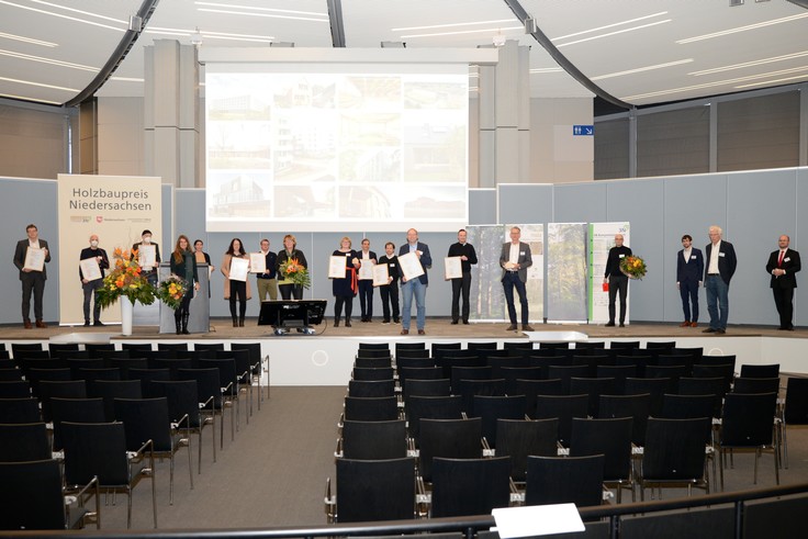 Alle Beteiligten des Holzbaupreises Niedersachsen stehen auf einer Bühne, die Preisträger mit Urkunden in der Hand.