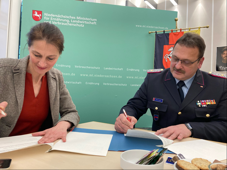 Forstministerin Miriam Staudte und Olaf Kapke sitzen am Tisch und unterzeichnen die Vereinbarung zur Aufklärungskampagne..