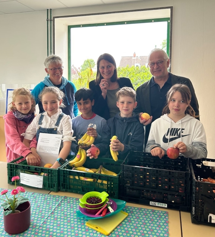 Gruppenbild vor Obstkisten: Ministerin Miriam Staudte mit Lehrerin Elisabeth Buß, Schulleiter Andreas Reichert und fünf Schülerinnen und Schülern.