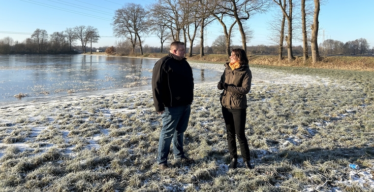 Ein Foto zeigt Ministerin Miriam Staudte im Austausch mit Landwirt Janek Böschen aus Grasberg im Landkreis Osterholz. Beide stehen auf einer überschwemmten Wiese, die teilweise auch von Schnee bedeckt ist.