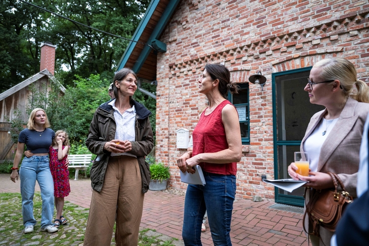 Ministerin Staudte im Gespräch mit Frau Cohrs vor einem roten Backsteingebäude.