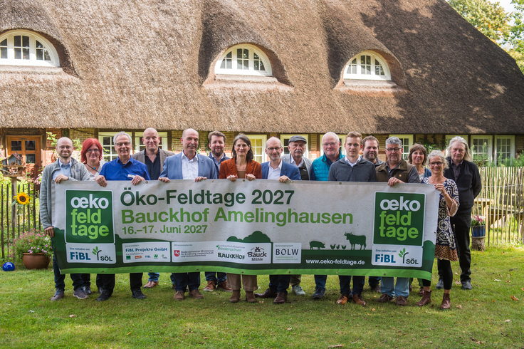Gruppenbild auf der grünen Wiese. Veranstalter halten ein Banner in der Hand.