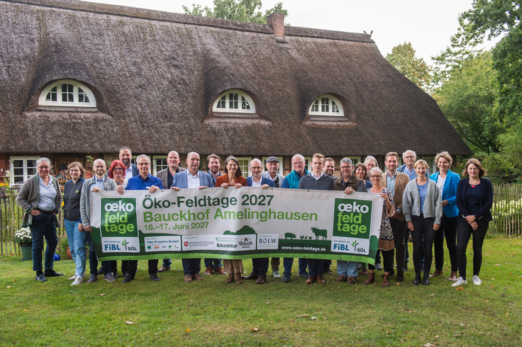 Gruppenbild auf der grünen Wiese. Es wird ein Banner der Ökofeldtage in den Händen gehalten.