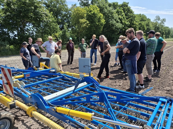 Landwirtinnen und Landwirte stehen auf einem Acker und hören dem Vortragenden vor