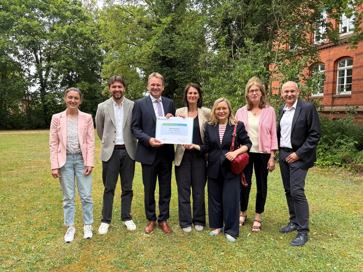 Ministerin Staudte übergibt eine Urkunde an Vertreterinnen und Vertreter der Dorfregion stehend auf einer grünen Wiese