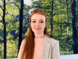 Junge Frau mit rotblonden Haaren vor einem Bild mit Wald