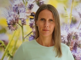 Frau mit langen Haaren und grünen Oberteil vor blauen Blumen