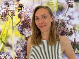 Junge Frau mit langen blonden Haaren und mit gestreiftem Oberteil vor Blumen-Hintergrund