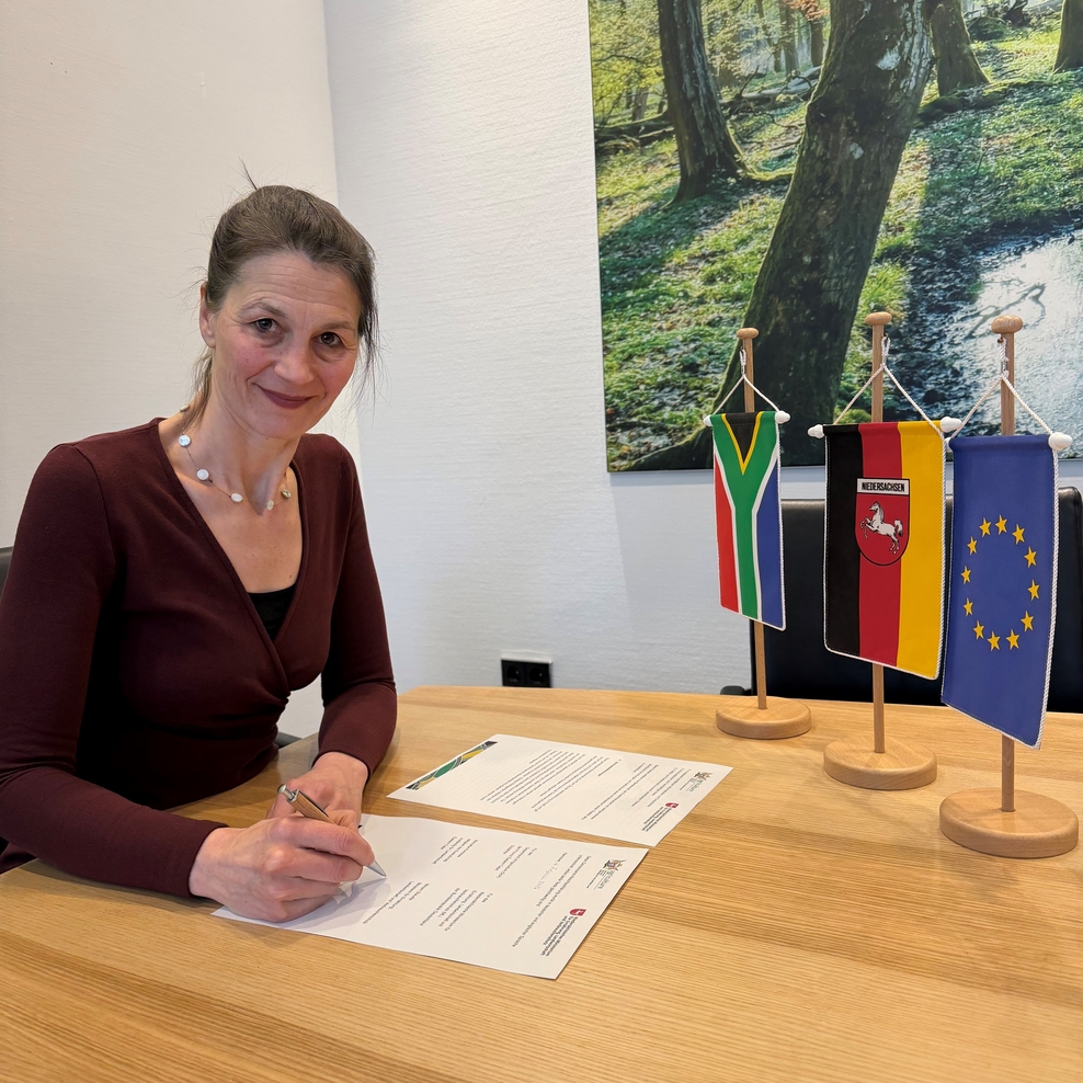 Ministerin Miriam Staudte sitzt am Besprechungstisch in ihrem Büro und unterzeichnet die Vereinbarung